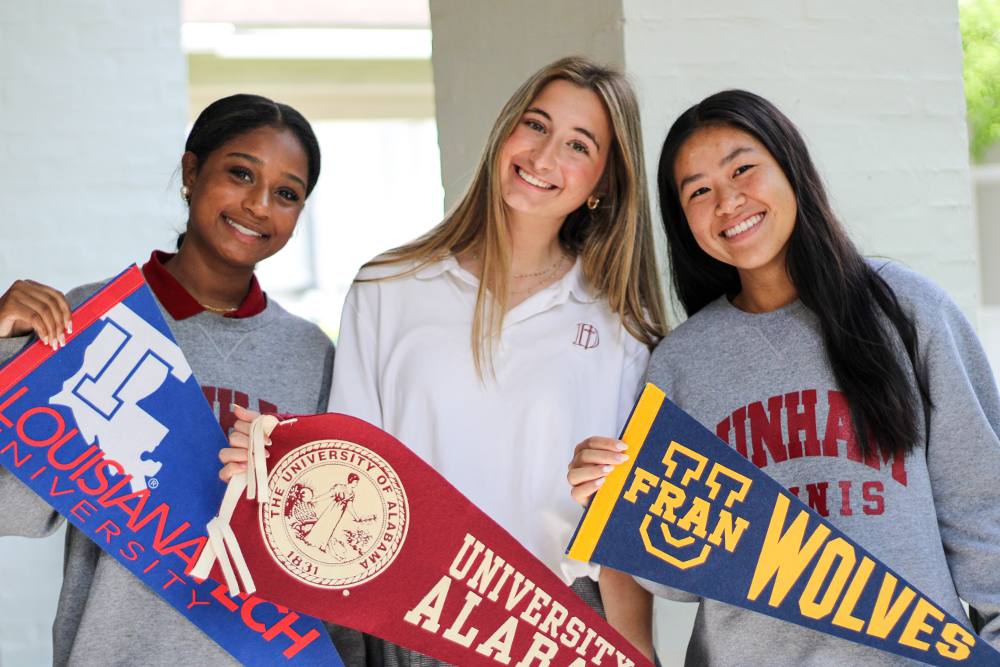 Three students holding up college acceptance pennants. 