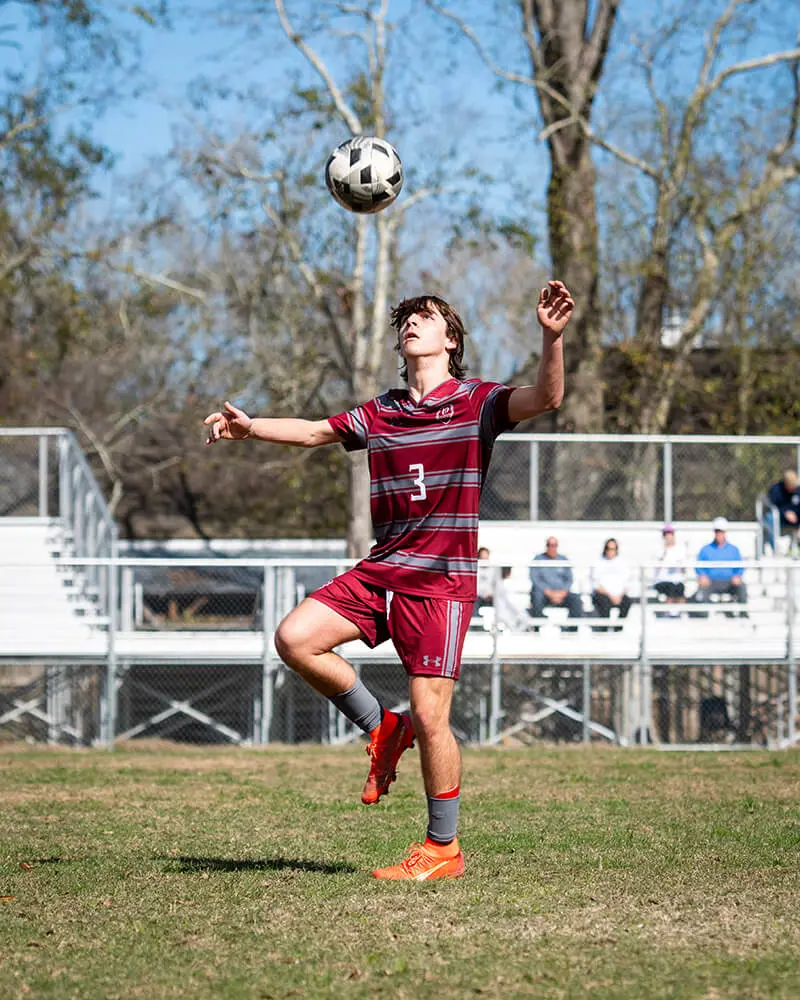 Varsity boys soccer player kicking soccer ball