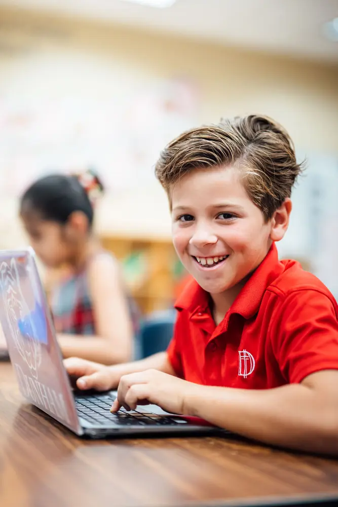 Lower school student working on schoolwork with MacBook laptop.